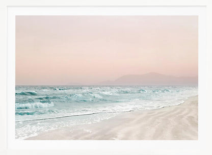 A serene coastal scene with gentle turquoise waves washing onto a sandy beach. The sky is a soft, hazy pink, and faint outlines of mountains are visible in the distant background. The artwork is presented in a silver frame. Print