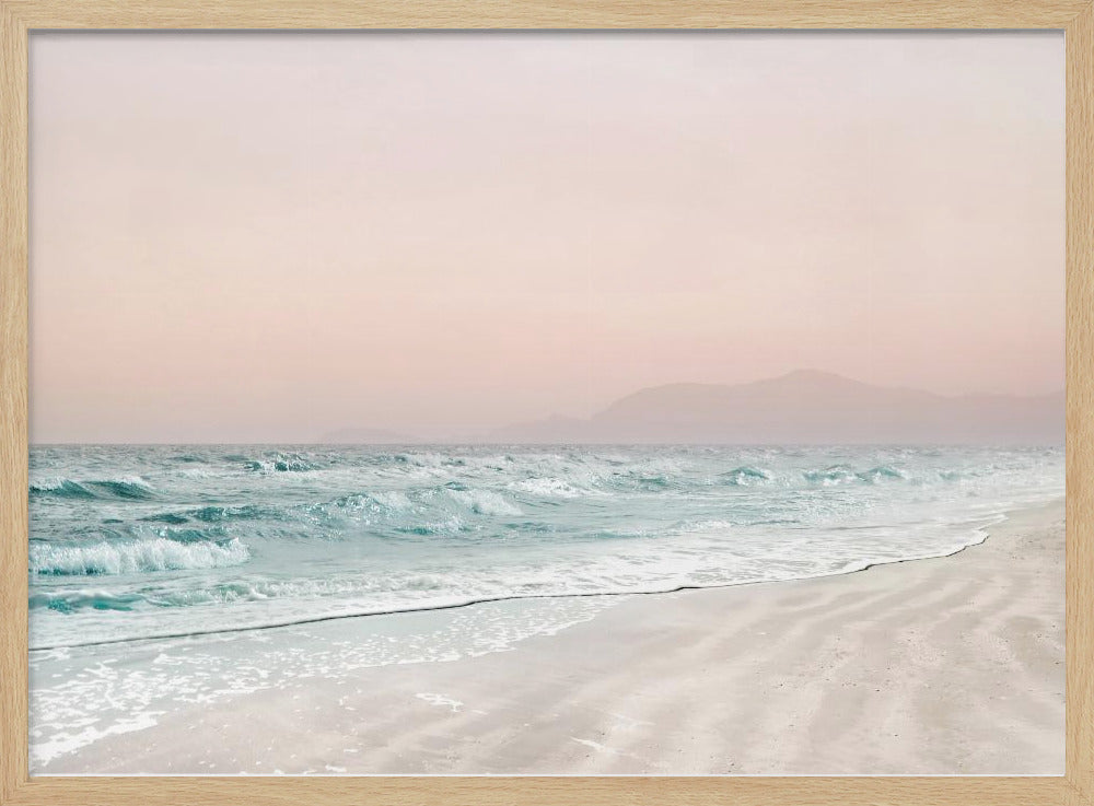 A serene coastal scene with gentle turquoise waves washing onto a sandy beach. The sky is a soft, hazy pink, and faint outlines of mountains are visible in the distant background. The artwork is presented in a silver frame. Print