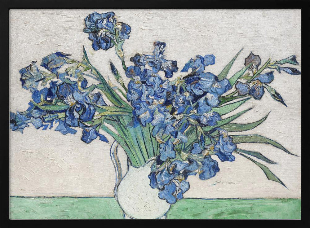 A framed print of Vincent van Gogh's famous painting 'Irises'. It features a large bouquet of vibrant blue iris flowers with long green leaves, arranged in a simple white pitcher. The background is a textured off-white wall, and the pitcher rests on a light green surface. The painting is in the post-impressionist style with thick, visible brushstrokes. Wall Art