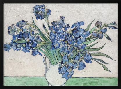 A framed print of Vincent van Gogh's famous painting 'Irises'. It features a large bouquet of vibrant blue iris flowers with long green leaves, arranged in a simple white pitcher. The background is a textured off-white wall, and the pitcher rests on a light green surface. The painting is in the post-impressionist style with thick, visible brushstrokes. Wall Art