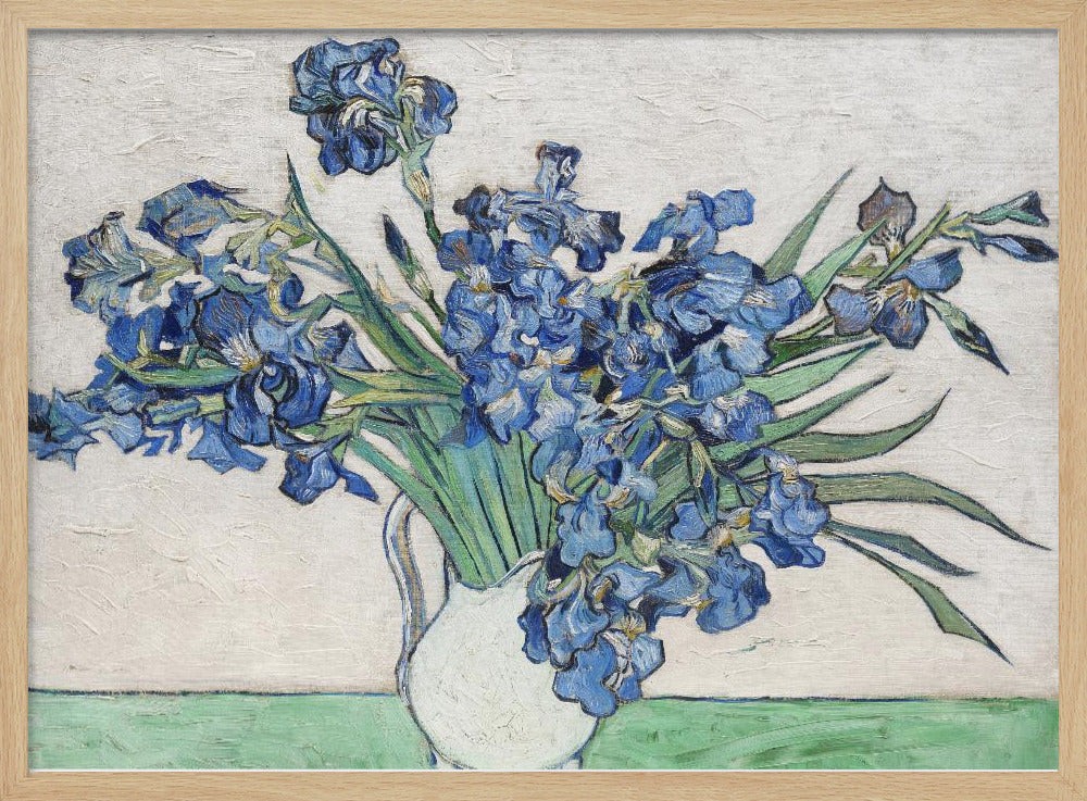 A framed print of Vincent van Gogh's famous painting 'Irises'. It features a large bouquet of vibrant blue iris flowers with long green leaves, arranged in a simple white pitcher. The background is a textured off-white wall, and the pitcher rests on a light green surface. The painting is in the post-impressionist style with thick, visible brushstrokes. Wall Art