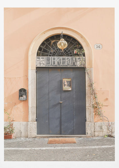 A charming European bookstore entrance featuring a large, dark grey arched door set against a peach-colored wall. Above the door, a sign reads 'LIBRERIA' below a decorative fanlight window and a hanging lantern. Decor