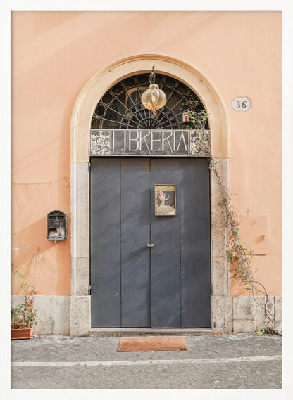 A charming European bookstore entrance featuring a large, dark grey arched door set against a peach-colored wall. Above the door, a sign reads 'LIBRERIA' below a decorative fanlight window and a hanging lantern. Decor