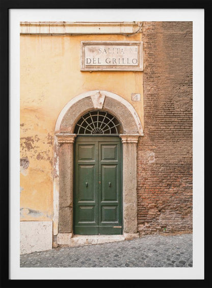 A vertical shot of a rustic European street scene featuring a dark green arched wooden door set into a stone frame. The building's facade is a mix of peeling yellow ochre plaster and exposed red brick. Above the door is a marble plaque that reads 'SALITA RI DEL GRILLO', and the ground is paved with grey cobblestones. Wall Art