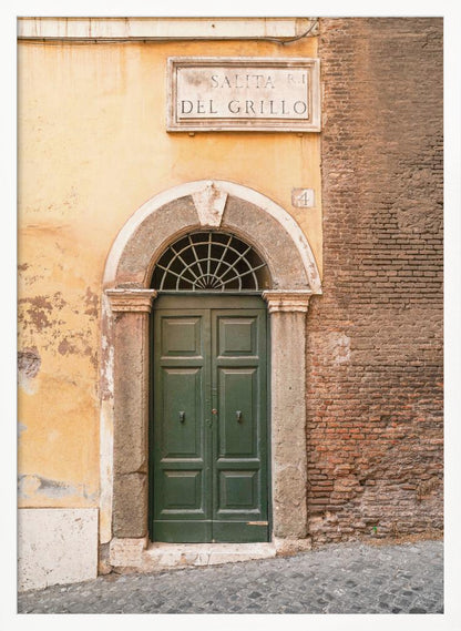 A vertical shot of a rustic European street scene featuring a dark green arched wooden door set into a stone frame. The building's facade is a mix of peeling yellow ochre plaster and exposed red brick. Above the door is a marble plaque that reads 'SALITA RI DEL GRILLO', and the ground is paved with grey cobblestones. Wall Art