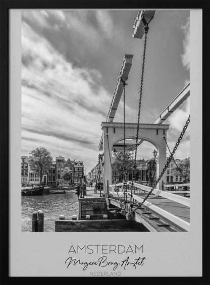 A black and white travel poster of Amsterdam, featuring a side view of the Magere Brug, a traditional wooden drawbridge, over the Amstel river. Classic canal houses line the waterway in the background under a dramatic, cloudy sky. The image is in a black frame and has text at the bottom that reads 'AMSTERDAM', 'Magere Brug, Amstel', and 'NEDERLAND'. Artwork