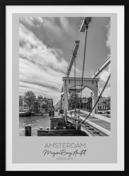 A black and white travel poster of Amsterdam, featuring a side view of the Magere Brug, a traditional wooden drawbridge, over the Amstel river. Classic canal houses line the waterway in the background under a dramatic, cloudy sky. The image is in a black frame and has text at the bottom that reads 'AMSTERDAM', 'Magere Brug, Amstel', and 'NEDERLAND'. Artwork