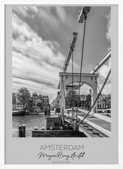 A black and white travel poster of Amsterdam, featuring a side view of the Magere Brug, a traditional wooden drawbridge, over the Amstel river. Classic canal houses line the waterway in the background under a dramatic, cloudy sky. The image is in a black frame and has text at the bottom that reads 'AMSTERDAM', 'Magere Brug, Amstel', and 'NEDERLAND'. Artwork