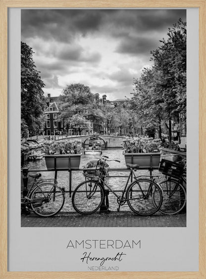 A black and white poster of the Herengracht canal in Amsterdam. In the foreground, two bicycles are parked by a railing with flower boxes. In the background, there's a classic view of the canal with a bridge, canal houses, and boats under a cloudy sky. The bottom of the poster has text that reads 'AMSTERDAM Herengracht NEDERLAND'. Decor