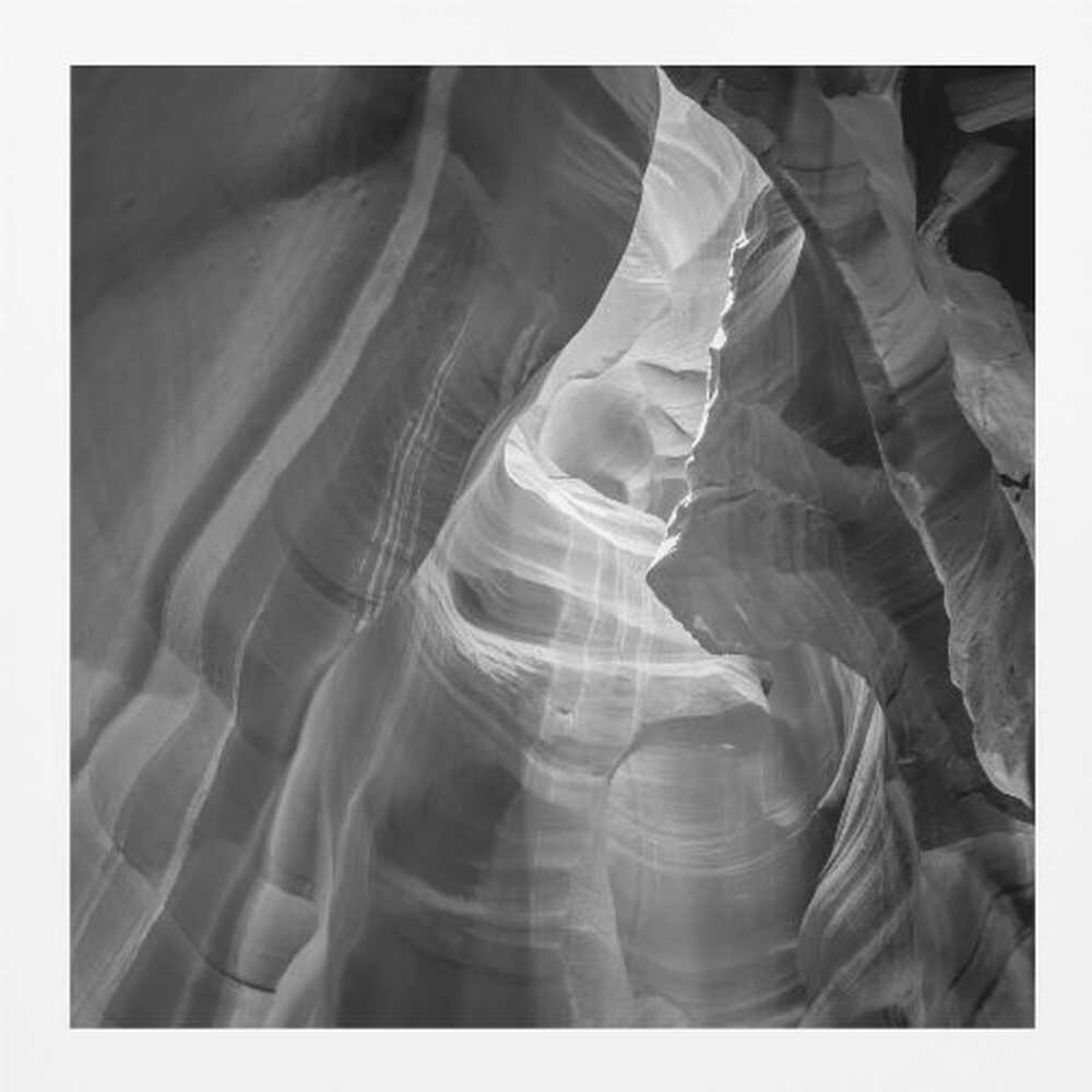 Black and white photo of light in a narrow slot canyon, highlighting smooth, layered rock formations. Nature wall art.