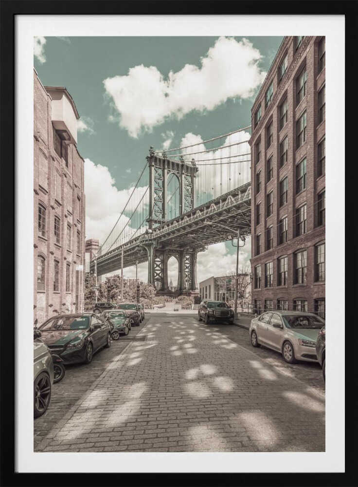 A vertical photograph of the Manhattan Bridge from a cobblestone street in DUMBO, Brooklyn, framed by tall brick buildings. The image has a vintage aesthetic with a muted teal sky and sepia-toned buildings and streets. Print