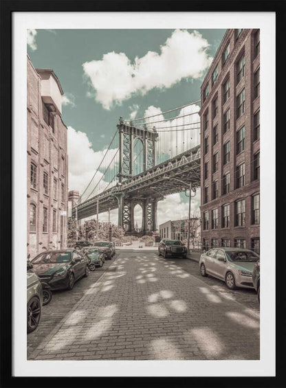 A vertical photograph of the Manhattan Bridge from a cobblestone street in DUMBO, Brooklyn, framed by tall brick buildings. The image has a vintage aesthetic with a muted teal sky and sepia-toned buildings and streets. Print