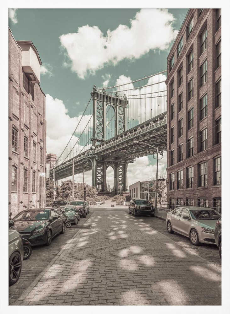 A vertical photograph of the Manhattan Bridge from a cobblestone street in DUMBO, Brooklyn, framed by tall brick buildings. The image has a vintage aesthetic with a muted teal sky and sepia-toned buildings and streets. Print