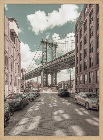 A vertical photograph of the Manhattan Bridge from a cobblestone street in DUMBO, Brooklyn, framed by tall brick buildings. The image has a vintage aesthetic with a muted teal sky and sepia-toned buildings and streets. Print