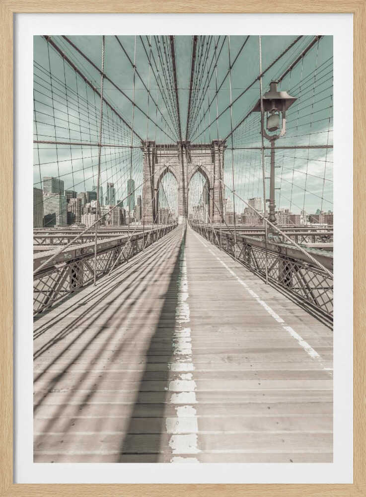 A vintage-style photograph looking down the center of the Brooklyn Bridge's wooden pedestrian walkway towards its iconic stone arches, with the New York City skyline visible in the background under a pale teal sky. The bridge's intricate network of suspension cables creates a strong sense of vanishing point perspective. Decor
