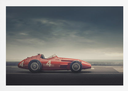 A side profile of a vintage red single-seater race car with the number 4 painted on it, parked on a seaside road under a dramatic, cloudy sky. The image has a muted, nostalgic color palette and is shown within a silver frame. Decor