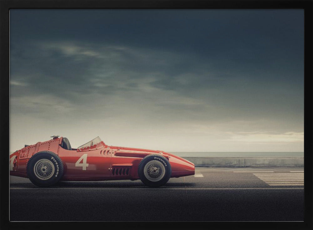 A side profile of a vintage red single-seater race car with the number 4 painted on it, parked on a seaside road under a dramatic, cloudy sky. The image has a muted, nostalgic color palette and is shown within a silver frame. Decor