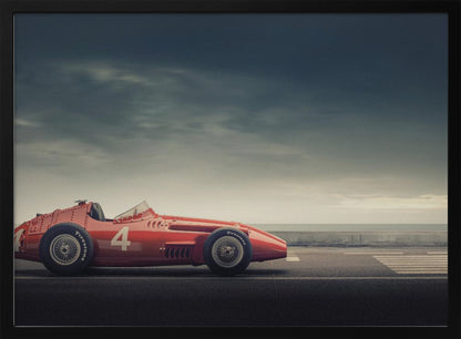 A side profile of a vintage red single-seater race car with the number 4 painted on it, parked on a seaside road under a dramatic, cloudy sky. The image has a muted, nostalgic color palette and is shown within a silver frame. Decor