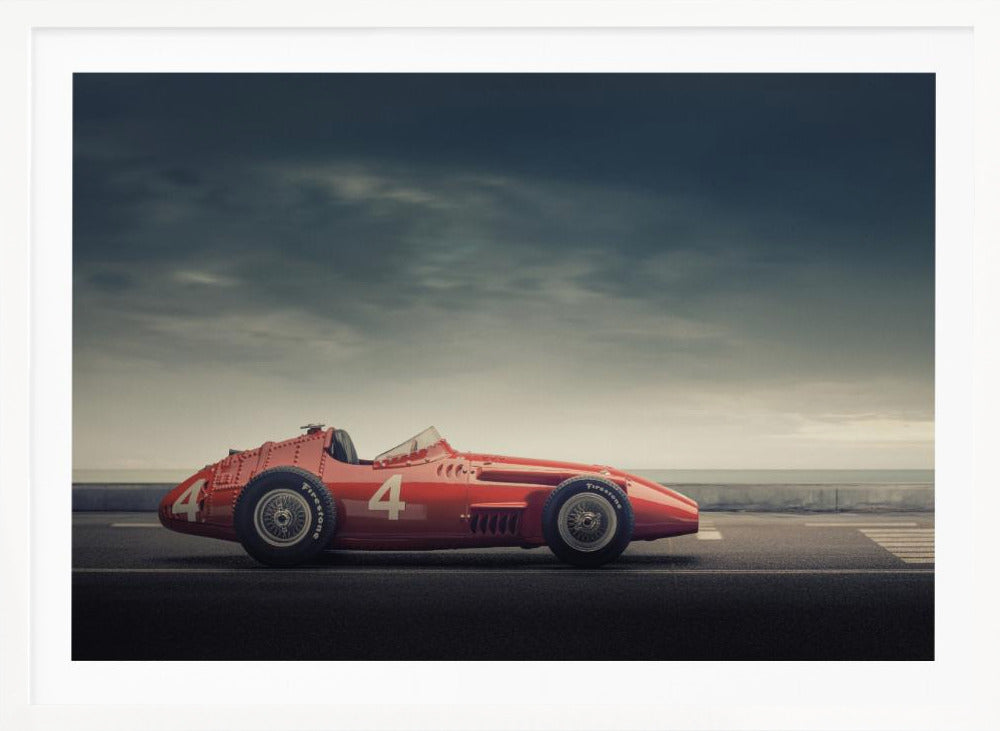 A side profile of a vintage red single-seater race car with the number 4 painted on it, parked on a seaside road under a dramatic, cloudy sky. The image has a muted, nostalgic color palette and is shown within a silver frame. Decor