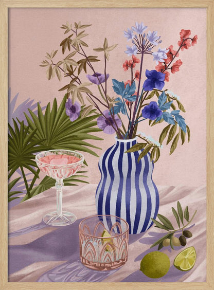 A vibrant still life painting featuring a blue and white striped wavy vase filled with a colorful bouquet of flowers. To the left is a pink cocktail in a coupe glass and a decorative tumbler. In the foreground, there are fresh limes and an olive branch. The scene is set on a draped pink cloth against a soft pink background with shadows from palm leaves. Artwork