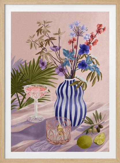 A vibrant still life painting featuring a blue and white striped wavy vase filled with a colorful bouquet of flowers. To the left is a pink cocktail in a coupe glass and a decorative tumbler. In the foreground, there are fresh limes and an olive branch. The scene is set on a draped pink cloth against a soft pink background with shadows from palm leaves. Artwork