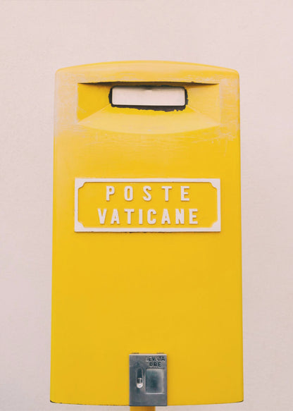 A close-up, front-view photograph of a vibrant yellow Vatican City mailbox against a plain beige wall, enclosed in a thin black frame. The words 'POSTE VATICANE' are printed in white on the front. Artwork