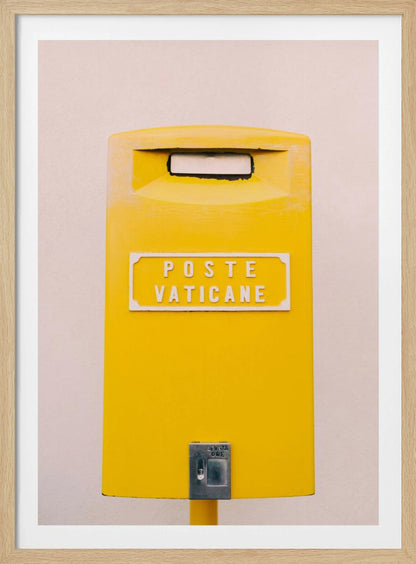 A close-up, front-view photograph of a vibrant yellow Vatican City mailbox against a plain beige wall, enclosed in a thin black frame. The words 'POSTE VATICANE' are printed in white on the front. Artwork