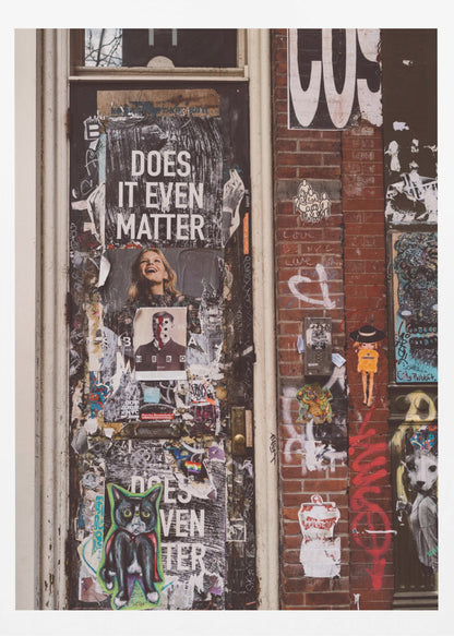 A close-up of a weathered dark door and an adjacent brick wall, both covered in a dense collage of street art, including peeling posters, stickers, and graffiti. A prominent poster on the door asks 'DOES IT EVEN MATTER' in bold white letters. Wall Art