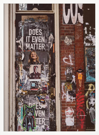 A close-up of a weathered dark door and an adjacent brick wall, both covered in a dense collage of street art, including peeling posters, stickers, and graffiti. A prominent poster on the door asks 'DOES IT EVEN MATTER' in bold white letters. Wall Art