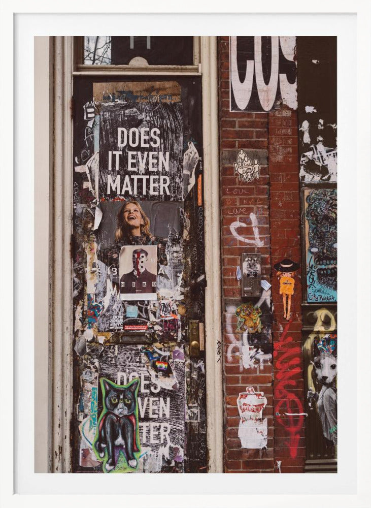 A close-up of a weathered dark door and an adjacent brick wall, both covered in a dense collage of street art, including peeling posters, stickers, and graffiti. A prominent poster on the door asks 'DOES IT EVEN MATTER' in bold white letters. Wall Art