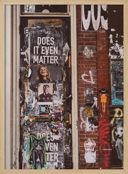 A close-up of a weathered dark door and an adjacent brick wall, both covered in a dense collage of street art, including peeling posters, stickers, and graffiti. A prominent poster on the door asks 'DOES IT EVEN MATTER' in bold white letters. Wall Art