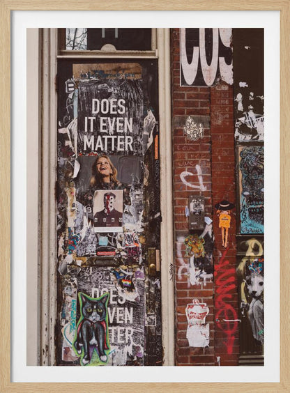 A close-up of a weathered dark door and an adjacent brick wall, both covered in a dense collage of street art, including peeling posters, stickers, and graffiti. A prominent poster on the door asks 'DOES IT EVEN MATTER' in bold white letters. Wall Art