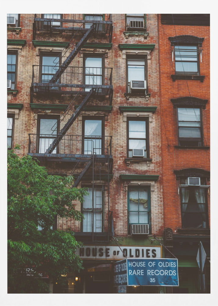 A classic multi-story brick apartment building with a prominent black metal fire escape zigzagging across its facade. A sign for a 'House of Oldies' rare records shop is visible on the ground floor. Poster