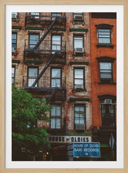 A classic multi-story brick apartment building with a prominent black metal fire escape zigzagging across its facade. A sign for a 'House of Oldies' rare records shop is visible on the ground floor. Poster