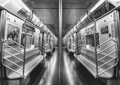 A framed, black and white photograph capturing a perfectly symmetrical view down the aisle of an empty subway car. The reflective, dark floor and the metallic seats and handrails create strong leading lines, giving the image a sense of depth and urban solitude. Wall Art
