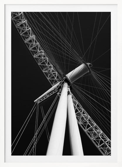 A dramatic low-angle, black and white photograph of a large Ferris wheel, focusing on the central hub and supporting structure. The image captures the white A-frame legs and the intricate lattice of the wheel's rim, with numerous tension cables radiating outwards against a solid black sky, creating a strong sense of perspective and geometric pattern. Artwork