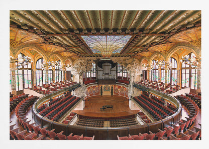 A high-angle, wide shot of the ornate and lavish interior of the Palau de la Música Catalana in Barcelona. The view captures the entire concert hall, with its curved balconies filled with red seats, a central wooden stage with a grand piano, and a spectacular, large stained-glass skylight in the ceiling. Poster