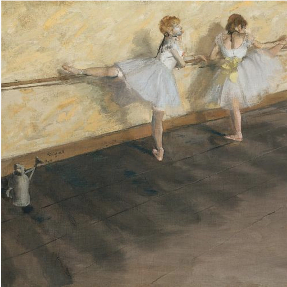 A framed impressionist painting by Edgar Degas depicting two ballet dancers in white tutus practicing at a barre. The studio has a yellow wall and a dark brown wooden floor. One dancer stretches her leg on the barre while the other stands beside her. Artwork