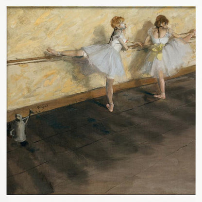 A framed impressionist painting by Edgar Degas depicting two ballet dancers in white tutus practicing at a barre. The studio has a yellow wall and a dark brown wooden floor. One dancer stretches her leg on the barre while the other stands beside her. Artwork