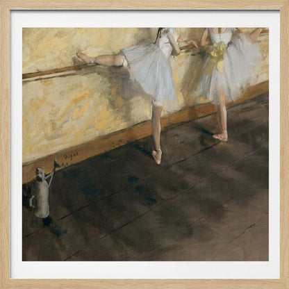 A framed impressionist painting by Edgar Degas depicting two ballet dancers in white tutus practicing at a barre. The studio has a yellow wall and a dark brown wooden floor. One dancer stretches her leg on the barre while the other stands beside her. Artwork