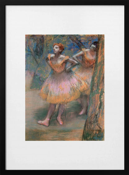 A framed vertical print of Edgar Degas's impressionist pastel drawing 'Dancers, Pink and Green'. It depicts two ballerinas in pink and orange tutus standing backstage amongst trees, captured in soft, expressive strokes. Artwork