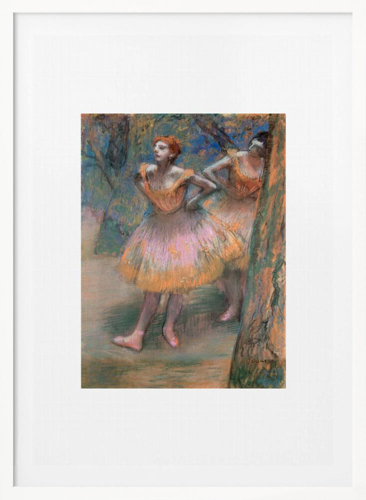 A framed vertical print of Edgar Degas's impressionist pastel drawing 'Dancers, Pink and Green'. It depicts two ballerinas in pink and orange tutus standing backstage amongst trees, captured in soft, expressive strokes. Artwork
