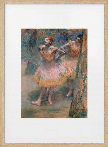 A framed vertical print of Edgar Degas's impressionist pastel drawing 'Dancers, Pink and Green'. It depicts two ballerinas in pink and orange tutus standing backstage amongst trees, captured in soft, expressive strokes. Artwork