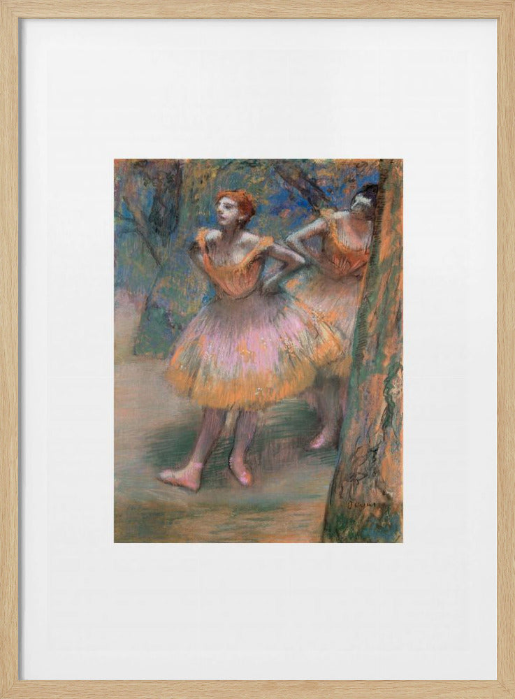 A framed vertical print of Edgar Degas's impressionist pastel drawing 'Dancers, Pink and Green'. It depicts two ballerinas in pink and orange tutus standing backstage amongst trees, captured in soft, expressive strokes. Artwork