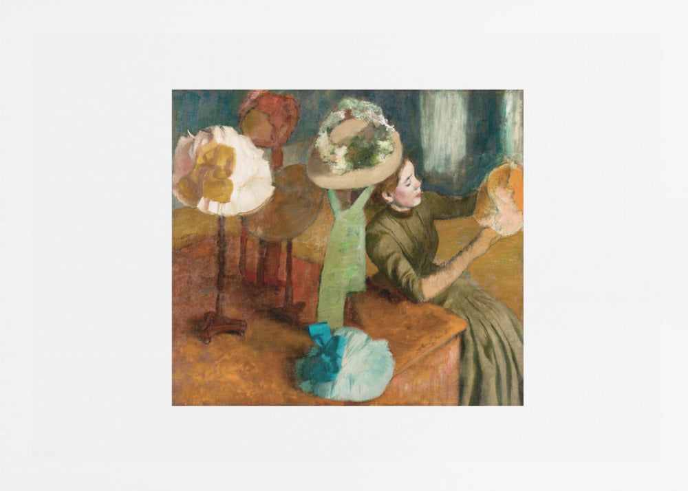 A framed print of Edgar Degas's Impressionist painting 'The Millinery Shop,' showing a woman in a green dress examining a hat in a shop filled with various fashionable hats on display stands. Print