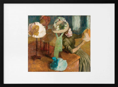 A framed print of Edgar Degas's Impressionist painting 'The Millinery Shop,' showing a woman in a green dress examining a hat in a shop filled with various fashionable hats on display stands. Print