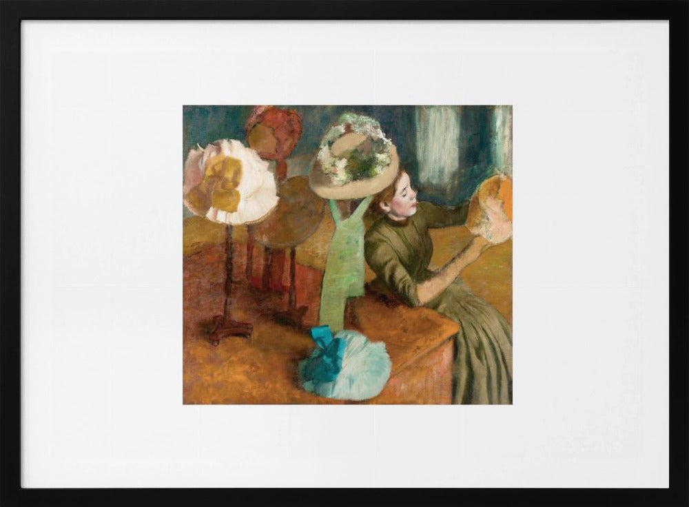 A framed print of Edgar Degas's Impressionist painting 'The Millinery Shop,' showing a woman in a green dress examining a hat in a shop filled with various fashionable hats on display stands. Print