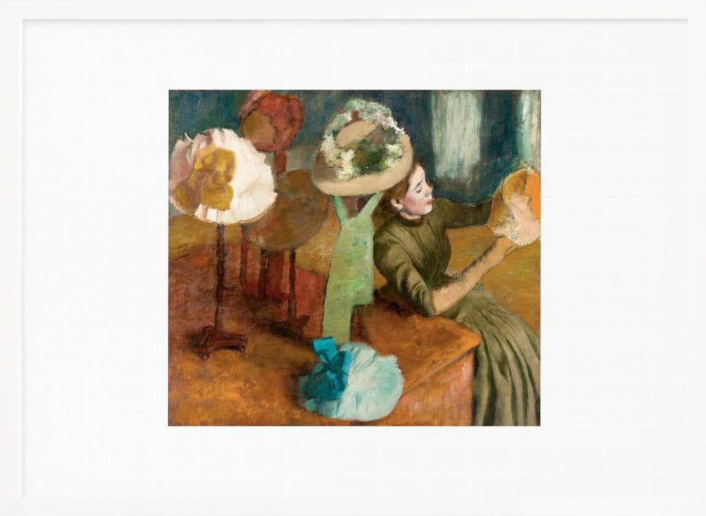A framed print of Edgar Degas's Impressionist painting 'The Millinery Shop,' showing a woman in a green dress examining a hat in a shop filled with various fashionable hats on display stands. Print