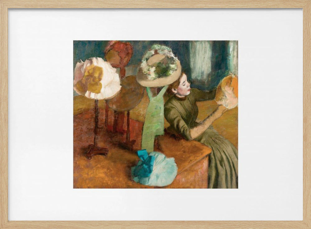 A framed print of Edgar Degas's Impressionist painting 'The Millinery Shop,' showing a woman in a green dress examining a hat in a shop filled with various fashionable hats on display stands. Print