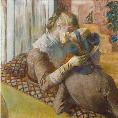 A framed Impressionist painting by Edgar Degas depicting two women. One woman, with blonde hair tied back, adjusts a hat with a blue ribbon on the other woman who is sitting with her back mostly to the viewer on a colorful patterned sofa. Print